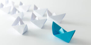 Concepto de liderazgo utilizando un barco de papel azul entre blancos.