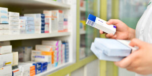 Farmacéutico sosteniendo una caja de medicamentos en una farmacia.