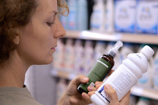 Cliente leyendo atentamente las etiquetas de dos productos de limpieza diferentes en un supermercado, comparando ingredientes y descripciones antes de tomar la decisión de compra.
