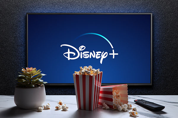 El logo de Disney+ en la televisión, con cajas de palomitas, control remoto y una planta sobre la mesa. Disney+ es un servicio estadounidense de streaming de video por suscripción.