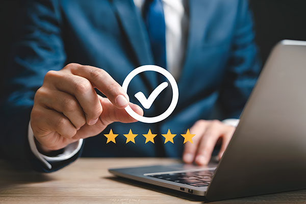 Persona de negocios que muestra una calificación de cinco estrellas cerca de una computadora portátil que representa una revisión en línea positiva y la satisfacción por el excelente servicio y la garantía de calidad en los negocios.