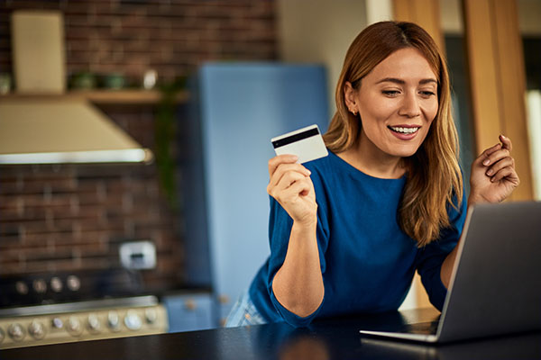 Una mujer feliz, estando en casa, usando una computadora portátil y comprando en línea, usando una tarjeta de crédito.