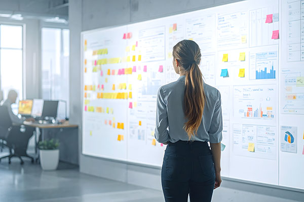 Mujer de espaldas trabajando en planificación estratégica con notas adhesivas en oficina moderna y luminosa.