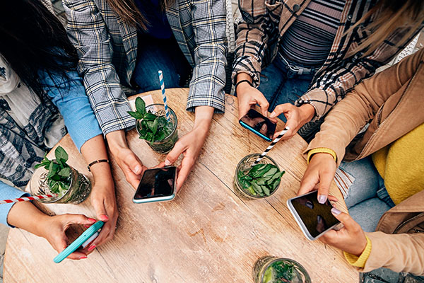 Grupo de manos femeninas usando un teléfono inteligente. Mujeres conectadas en línea. Vista superior de amigas multirraciales en círculo usando un teléfono wifi en una cafetería.