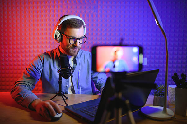Vlogger usando un smartphone para grabar un podcast en un estudio. Blogger con teléfono móvil, micrófono y auriculares grabando un vídeo para su carrera de difusión en redes sociales.