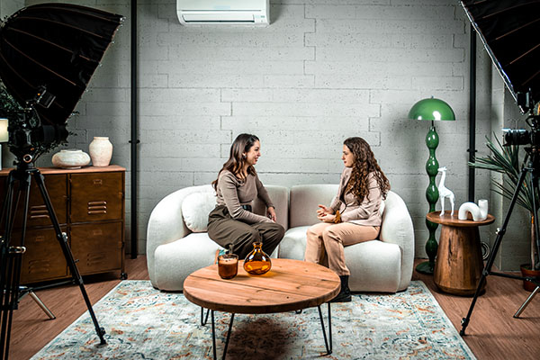 Dos mujeres presentan un podcast y conversan en un estudio profesional con cámaras y equipos de iluminación.