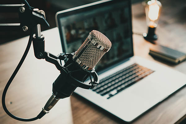 Interior de un estudio de podcast casero. Micrófono, portátil y lámpara de estar al aire sobre la mesa, primer plano.